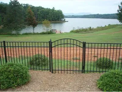 Black metal gate overlooking a grassy lawn and lake beyond