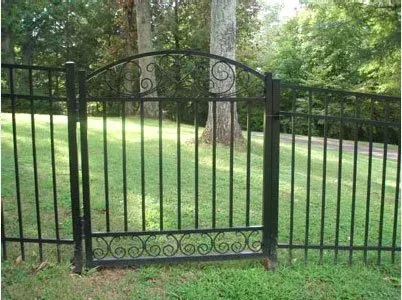 Black wrought-iron gate in a grassy yard with trees in the background