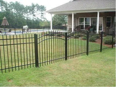 Black metal fence in front of a brick house with a covered patio and grassy yard.