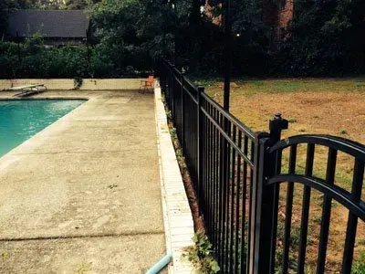 Poolside concrete patio beside black metal fence and dry grass yard