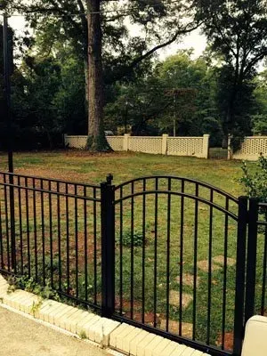 Black metal gate in front of a grassy yard with trees and a white fence.