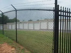 Chain-link fence and black metal gate beside a row of white storage units on a cloudy day
