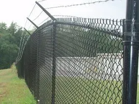 Chain-link fence topped with barbed wire, bent outward along a grassy roadside