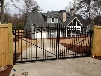Black metal driveway gate before a gray house with white trim and stone accents