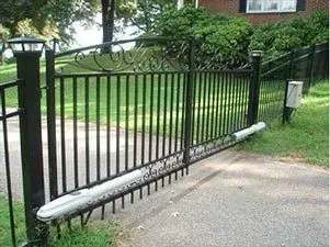 Black metal driveway gate with decorative top, partly open and bent at the bottom, in a suburban yard.