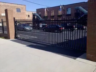 Black metal gate across a paved parking lot beside brick apartment buildings.