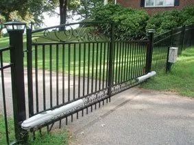 Black metal gate collapsed outward across a driveway beside a green lawn and brick building