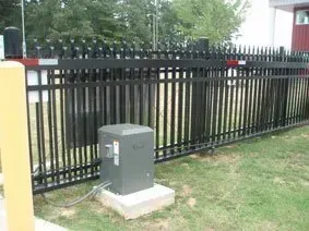Gray utility box on a concrete pad beside a black metal fence in a grassy yard