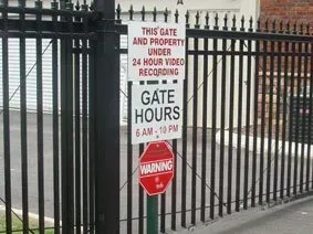Black metal gate with sign warning of 24-hour video recording and gate hours, 6 AM–10 PM.