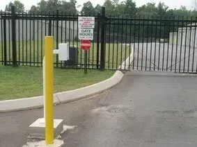 Yellow bollard and gated entrance with a “GATE CLOSES” sign by a paved driveway