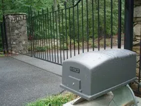 Gray mailbox beside a driveway gate and black metal fence in a suburban yard