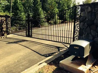 Black metal driveway gate beside a stone wall, with a mailbox on a concrete driveway