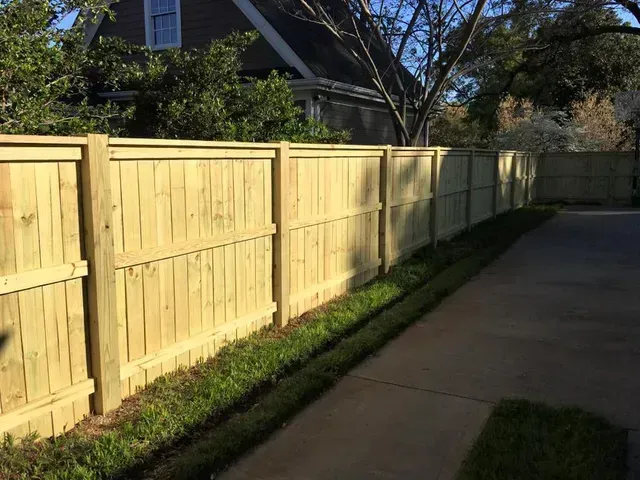 Wooden fence along a sidewalk beside a narrow strip of grass in bright sunlight