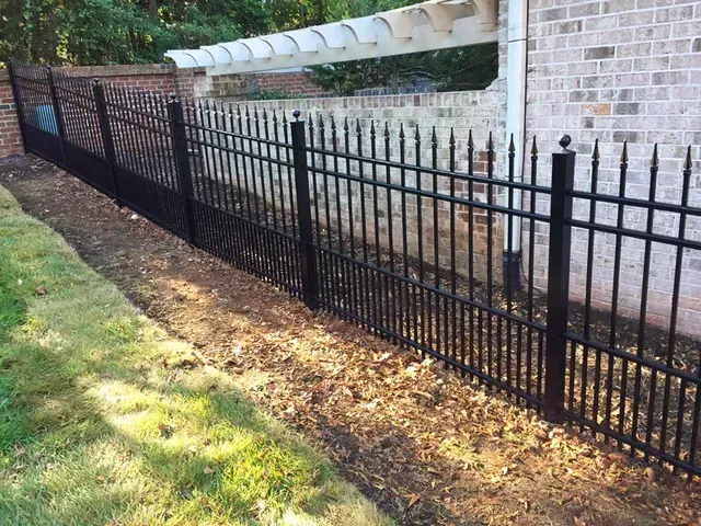 Black metal fence along a brick house beside a leafy yard and concrete walkway