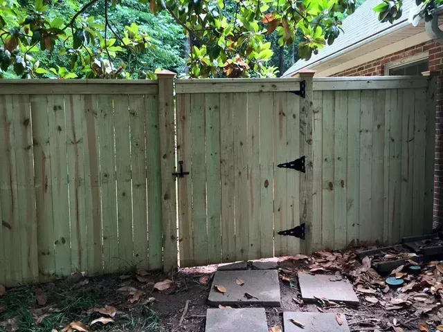 Wooden backyard fence gate with black hinges and stone pavers on the ground