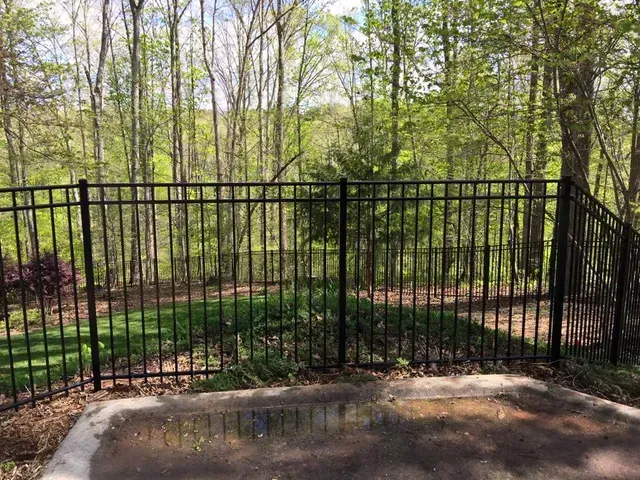 Black metal fence around a backyard patio with trees and a wooded area beyond