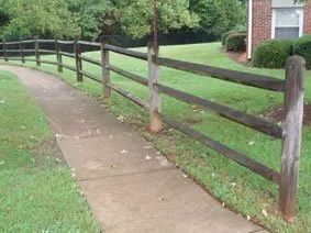 Curved sidewalk beside a wooden rail fence on a grassy residential path