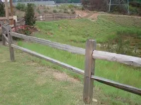 Wooden fence along a grassy rural path with fields in the background