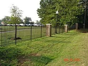 Black metal fence along a grassy field with stone posts and trees in the background