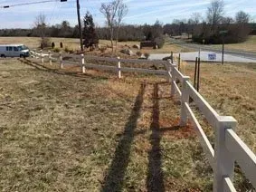 White fence along a grassy roadside field under a blue sky
