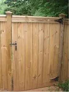 Wooden garden gate with black hinges and latch, set in a fence with trees behind it