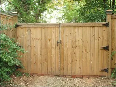 Wooden garden gate with black hinges and stone posts, surrounded by greenery