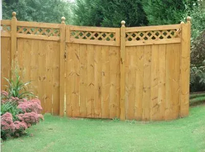 Curved wooden garden fence with lattice top panels beside grass and shrubs