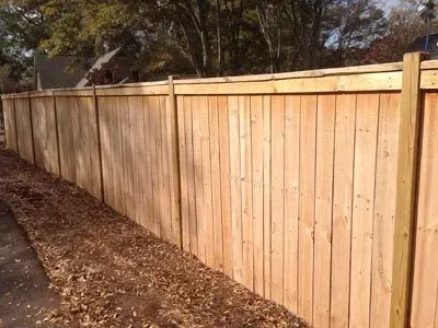 New wooden privacy fence along a dirt path beside trees and a house