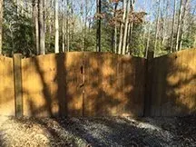 Wooden fence in a wooded backyard with sunlight and tree shadows.