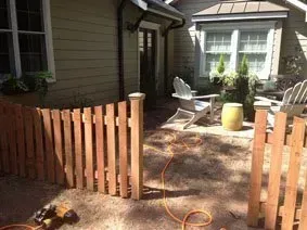 Backyard patio with wooden gate, white chairs, and an orange hose on the ground