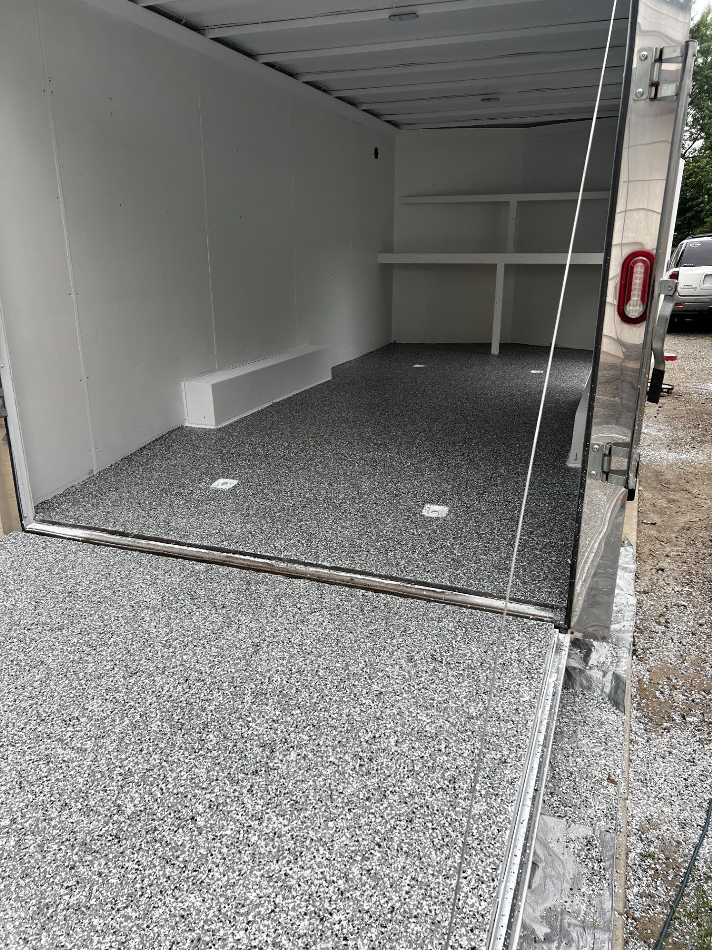 The open rear door of an enclosed trailer with a gray and white speckled epoxy floor and interior shelving.