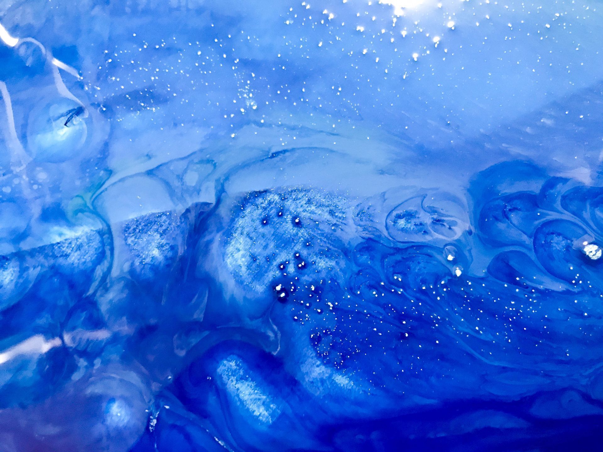 Abstract blue liquid swirl with varied shades, bubbles, and white specks, resembling flowing water or cosmic nebula.