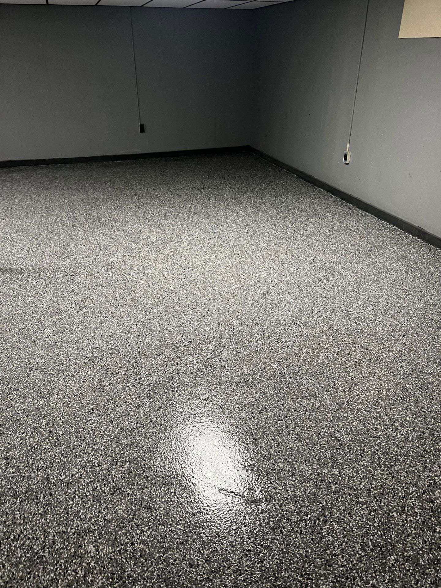 A basement room featuring a polished, dark gray and white speckled epoxy floor with dark walls.