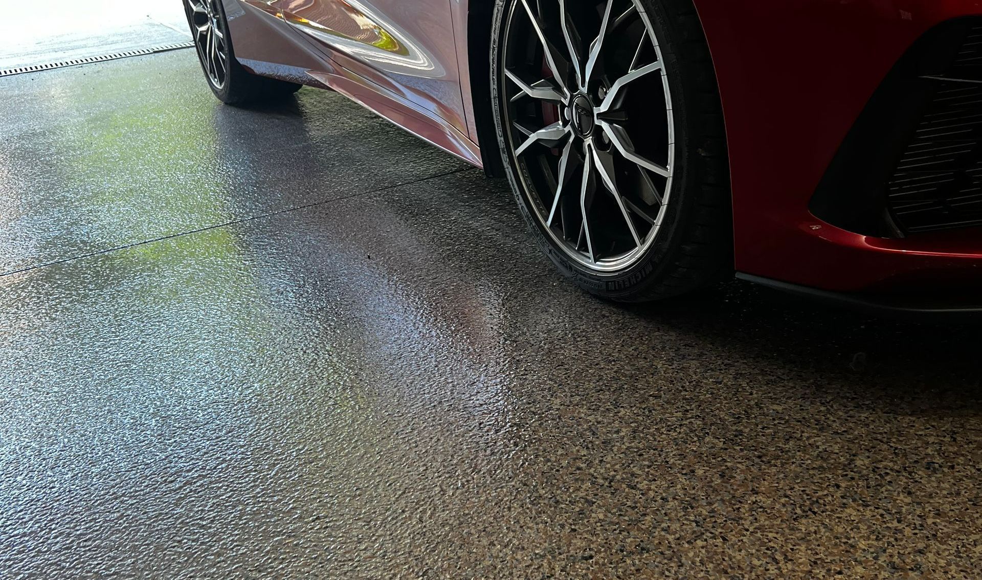 A red car parked on a gray speckled epoxy garage floor.