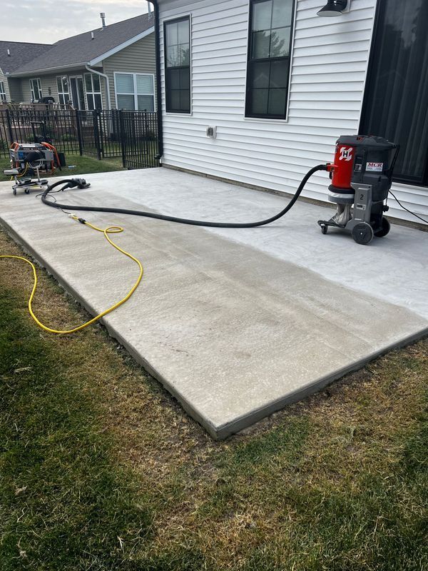 A concrete patio being ground and cleaned with an industrial vacuum and floor grinder against a house exterior.
