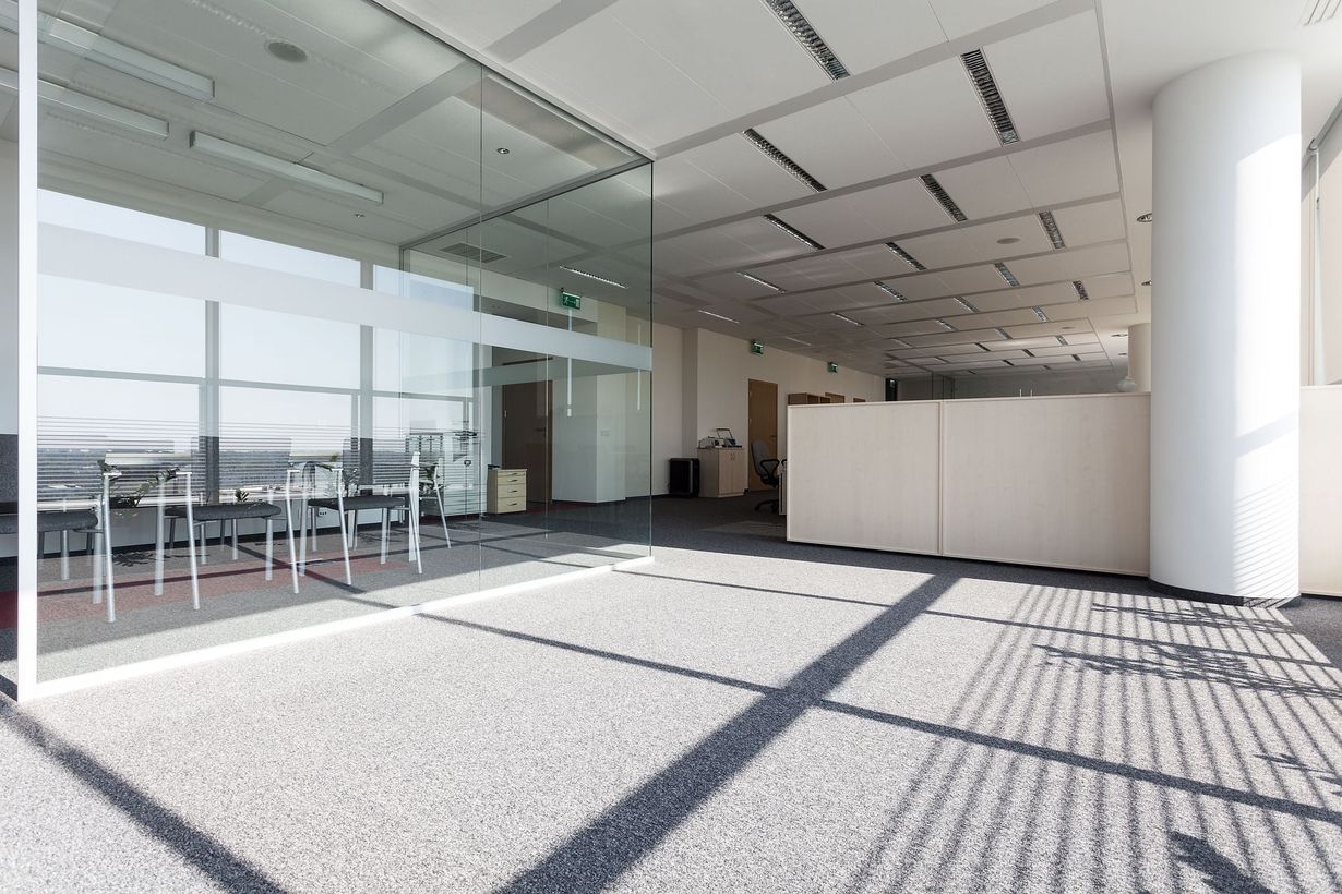 Empty, bright office space with a glass-walled meeting room, a large column, and textured flooring.