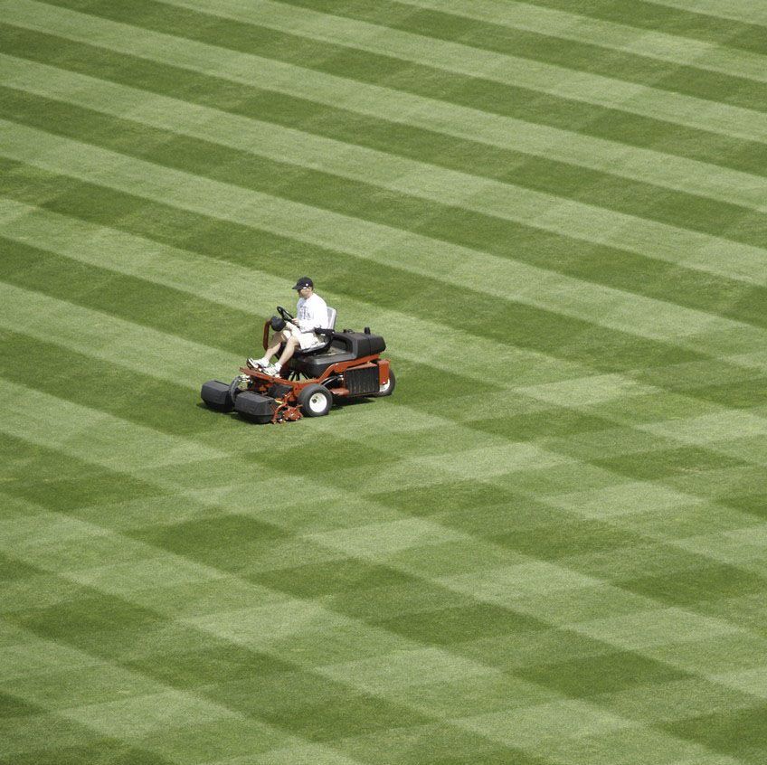 A man is riding a lawn mower on a baseball field.