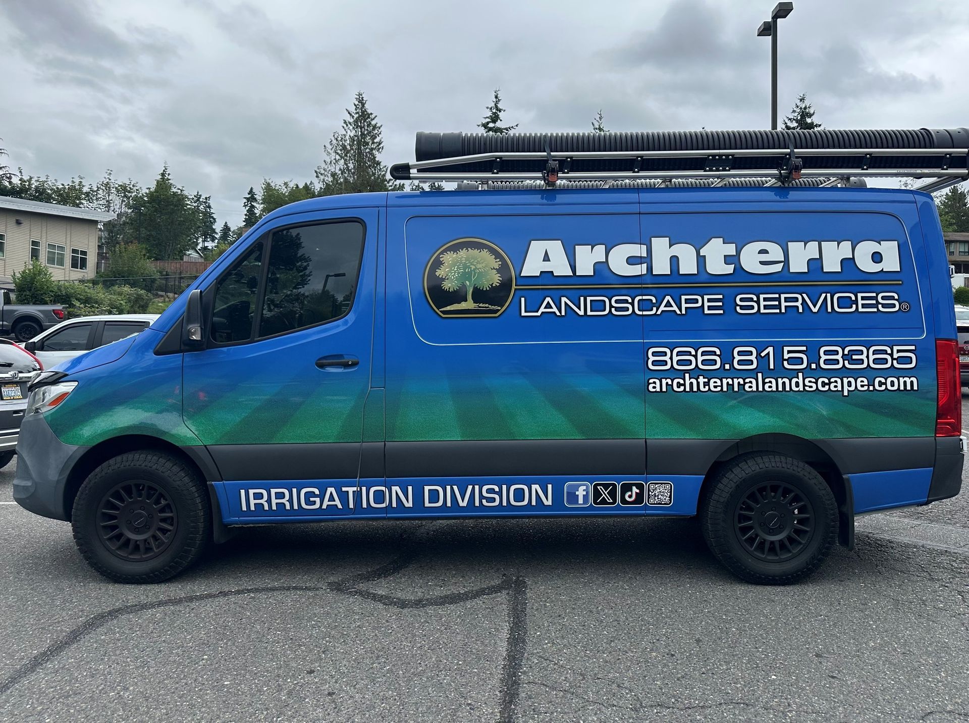 Blue work van with Archterra Landscape Services logo, parked outdoors.