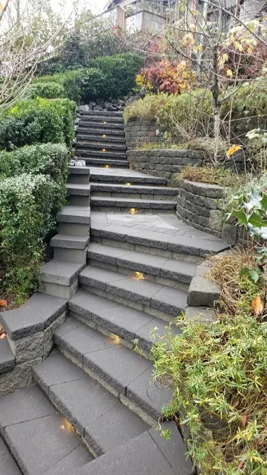 Stone stairs ascending a hillside, flanked by greenery and retaining walls.