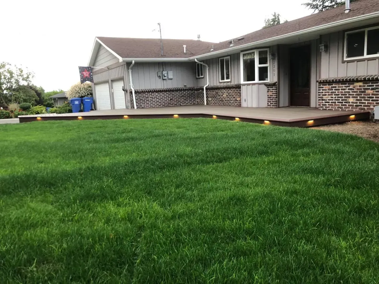 A house with a concrete patio and green lawn. The patio has yellow lights.