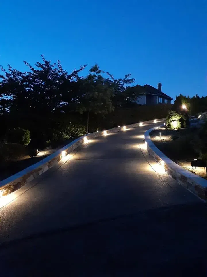 Dark driveway lit by small lights, leading to a house at dusk.