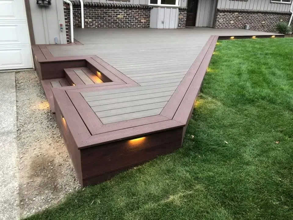 Wooden deck with steps, built-in lights, and brown trim, next to a green lawn.