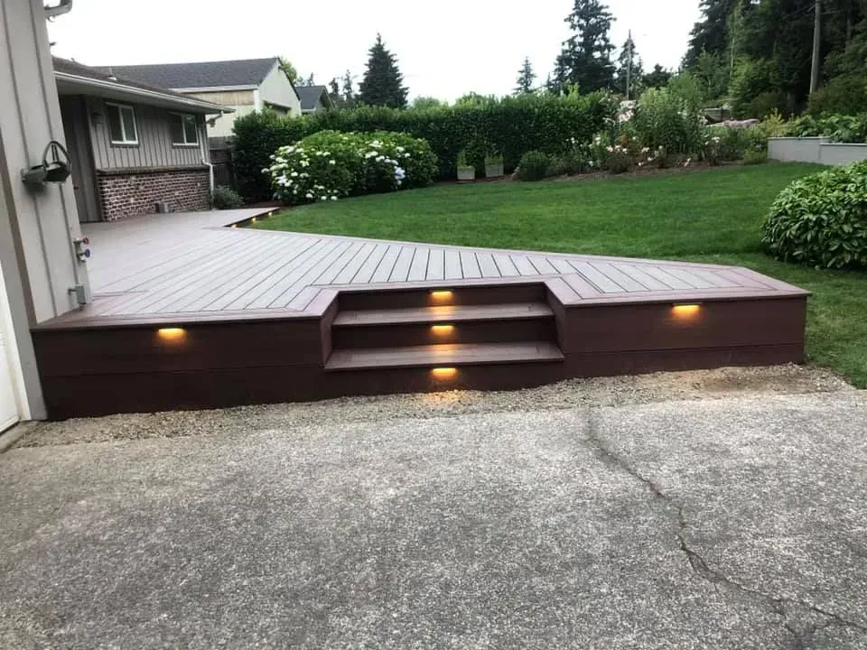 Brown deck with built-in steps and lights, leading to a lawn. A house is in the background.