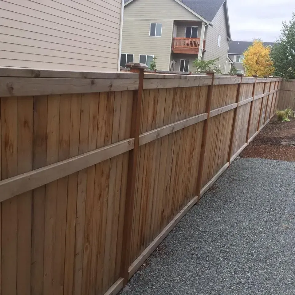 Wooden privacy fence in a backyard with a gravel ground, houses in the background.