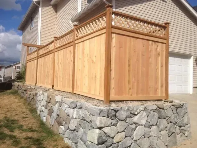 Wooden fence atop a stone retaining wall beside a house.