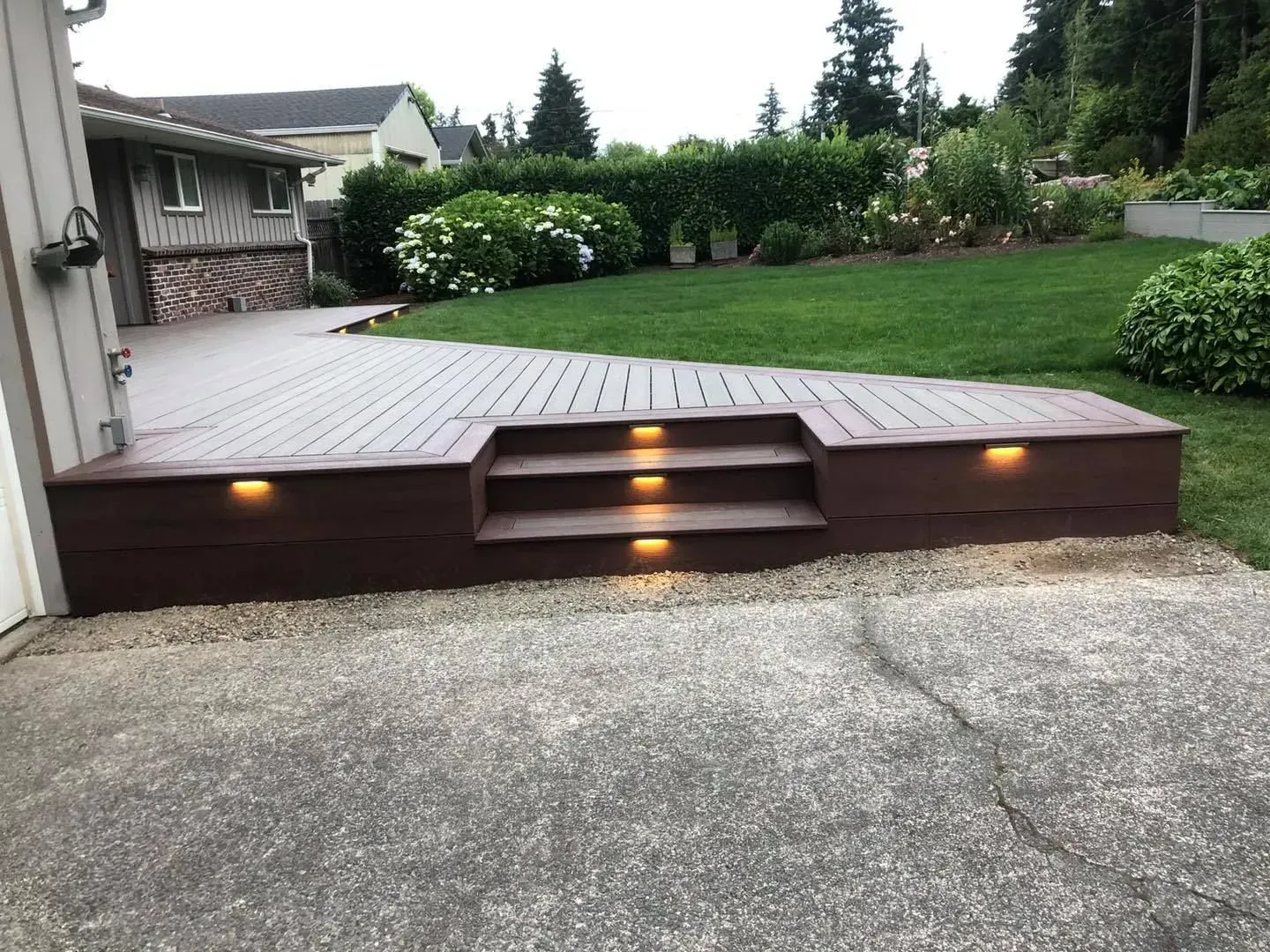 Brown composite deck with steps and built-in lights leading to a grassy yard from a concrete driveway.