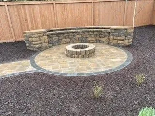 Stone fire pit with curved seating in a landscaped backyard.