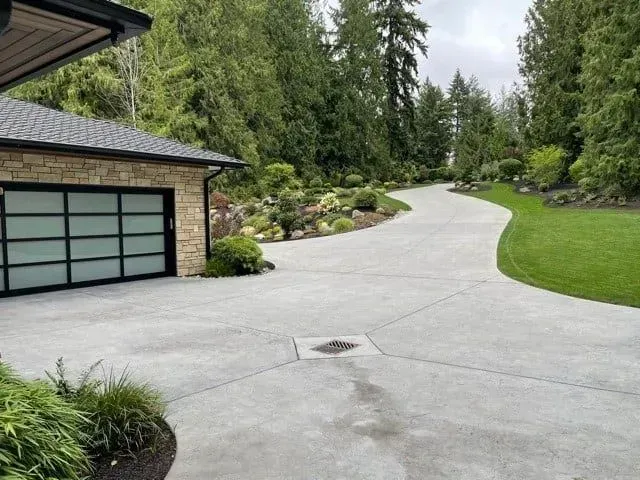 Driveway leading to a garage with a stone facade, surrounded by lush greenery.