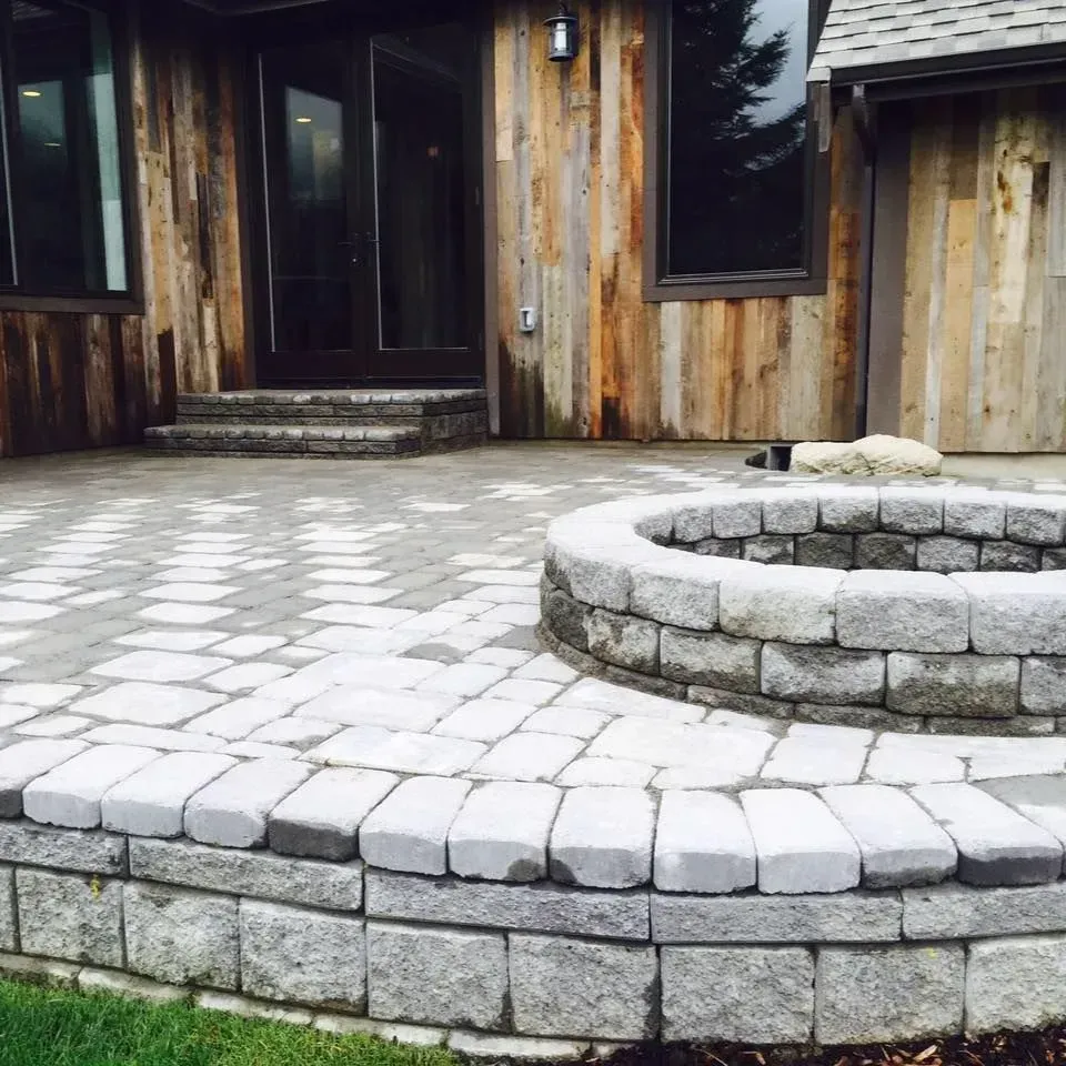 Stone patio with a fire pit in front of a wooden building, outdoors.