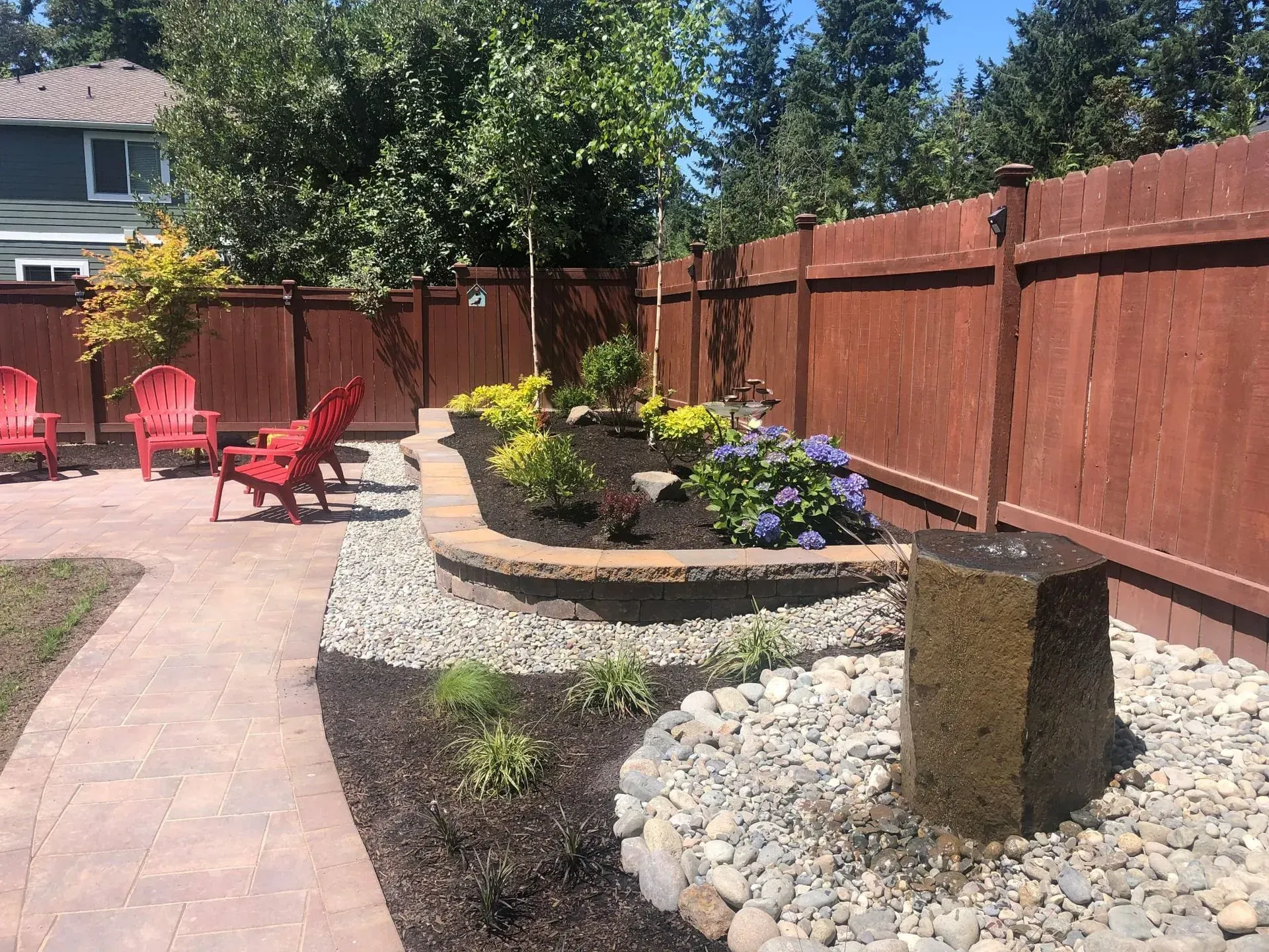 Backyard with red chairs, stone fountain, raised garden bed, and wood fence.